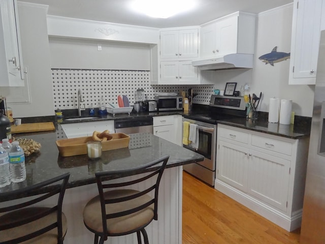 kitchen featuring white cabinets, appliances with stainless steel finishes, a kitchen bar, sink, and kitchen peninsula