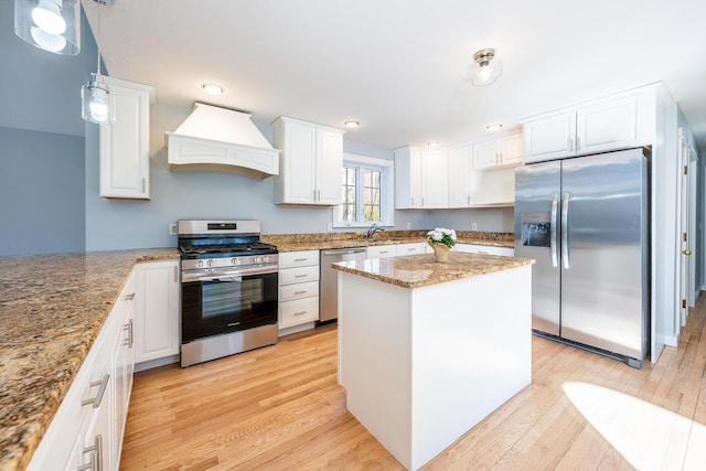 kitchen with custom range hood, light stone counters, decorative light fixtures, stainless steel appliances, and white cabinetry