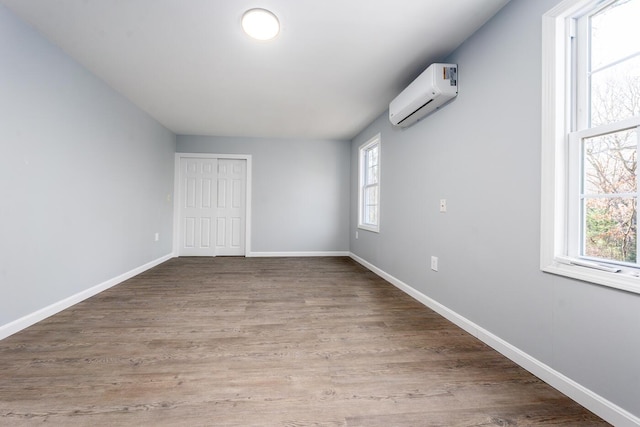 spare room featuring baseboards, an AC wall unit, and wood finished floors