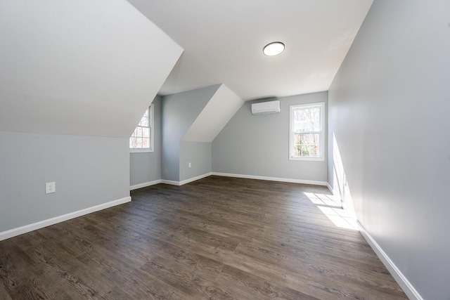 additional living space with lofted ceiling, dark wood-style flooring, a wall unit AC, and baseboards