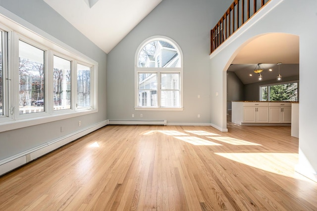 spare room featuring light wood-style floors, arched walkways, and a healthy amount of sunlight