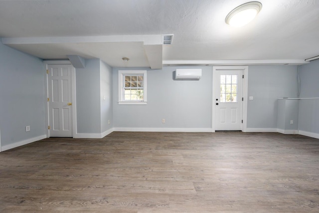 foyer entrance with an AC wall unit, plenty of natural light, baseboards, and wood finished floors