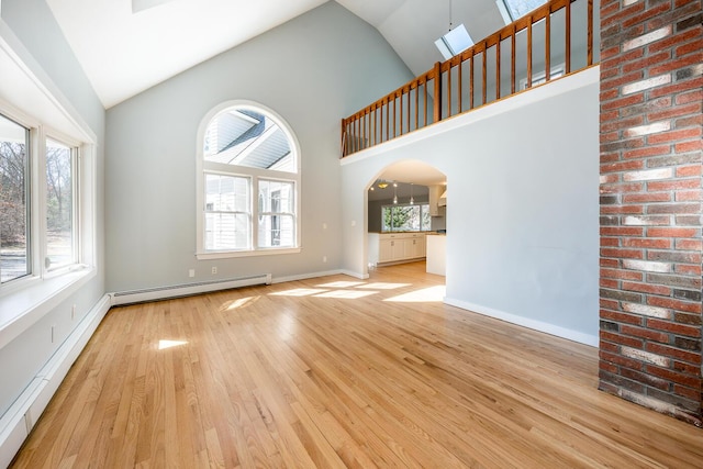 unfurnished living room with a baseboard heating unit, arched walkways, a healthy amount of sunlight, and light wood-style flooring