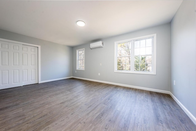 unfurnished bedroom with a wall unit AC, a closet, baseboards, and dark wood-style flooring