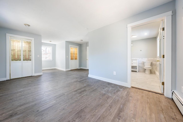 unfurnished living room featuring a baseboard radiator, baseboards, and wood finished floors