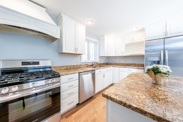 kitchen featuring stainless steel appliances, white cabinets, light stone counters, and custom exhaust hood