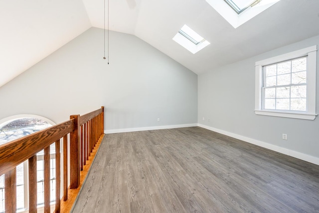 additional living space with lofted ceiling with skylight, baseboards, and wood finished floors