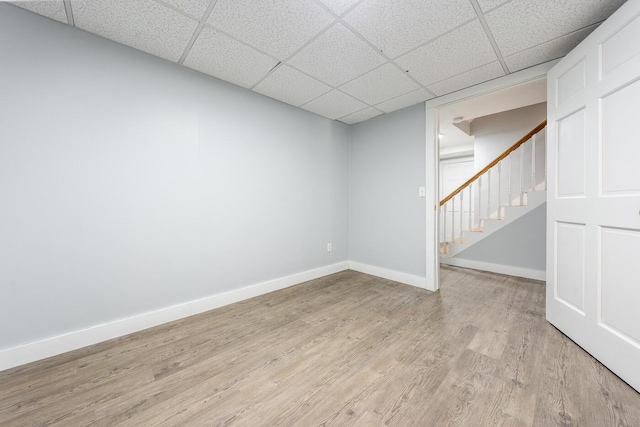 finished basement featuring stairway, light wood-type flooring, a paneled ceiling, and baseboards