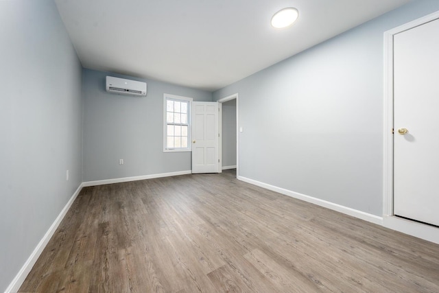 spare room featuring a wall mounted AC, wood finished floors, and baseboards