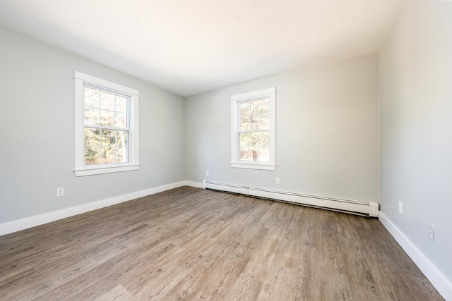 spare room with a baseboard heating unit, a healthy amount of sunlight, light wood finished floors, and baseboards