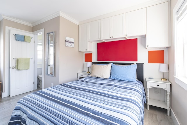 bedroom with light wood-type flooring, crown molding, and ensuite bath