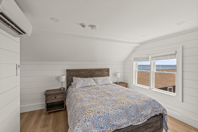 bedroom featuring hardwood / wood-style flooring, a water view, a wall mounted AC, and lofted ceiling