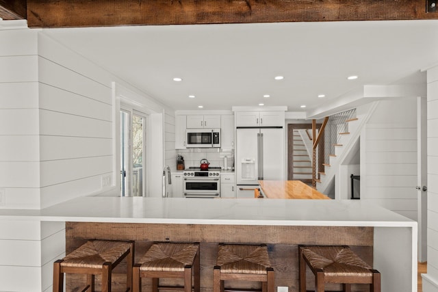 kitchen featuring a kitchen bar, white cabinetry, kitchen peninsula, and high end appliances