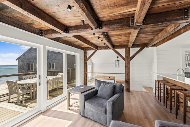 living room with wood ceiling, beamed ceiling, wood walls, a water view, and light hardwood / wood-style flooring