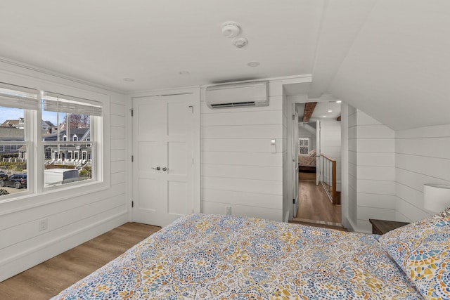 bedroom with light hardwood / wood-style floors, an AC wall unit, wood walls, and vaulted ceiling