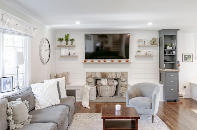 living room with wood-type flooring, ornamental molding, and a stone fireplace