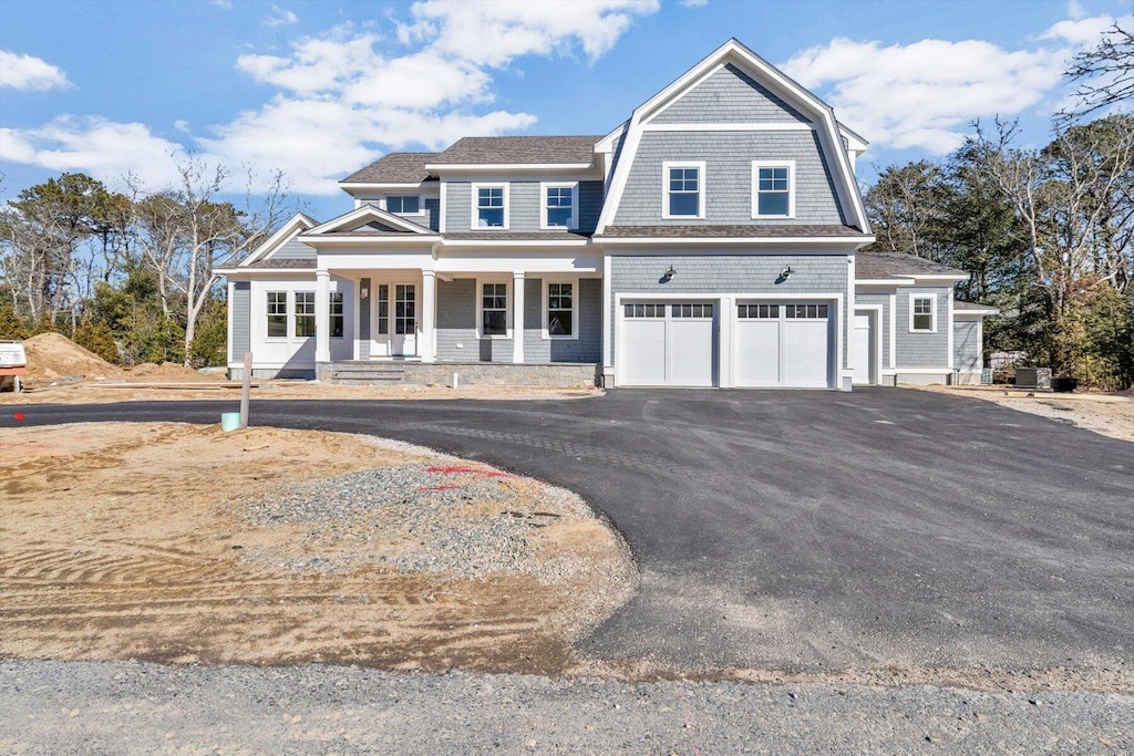 shingle-style home with covered porch, driveway, a gambrel roof, and a garage