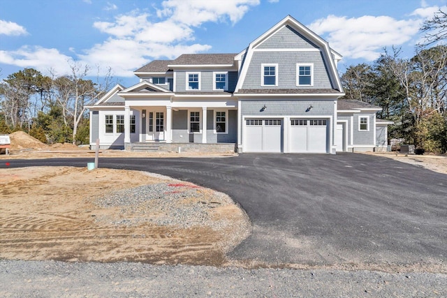 shingle-style home with a gambrel roof, a porch, driveway, and an attached garage