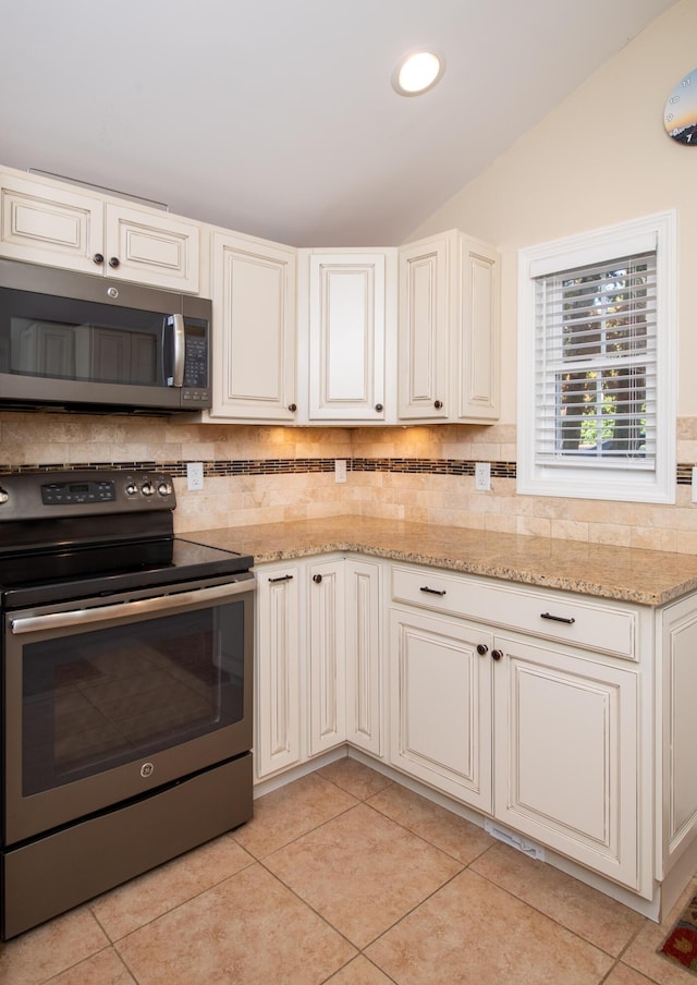 kitchen with light tile patterned floors, light stone countertops, lofted ceiling, and stainless steel appliances