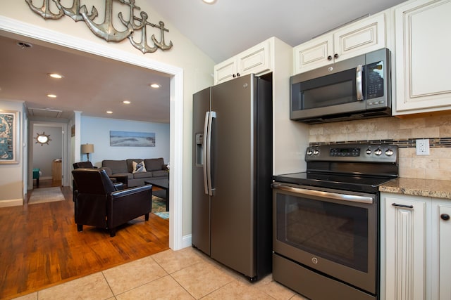 kitchen featuring white cabinets, lofted ceiling, stainless steel appliances, light tile patterned flooring, and light stone counters