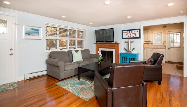 living room featuring a baseboard heating unit, dark hardwood / wood-style floors, crown molding, and a tiled fireplace