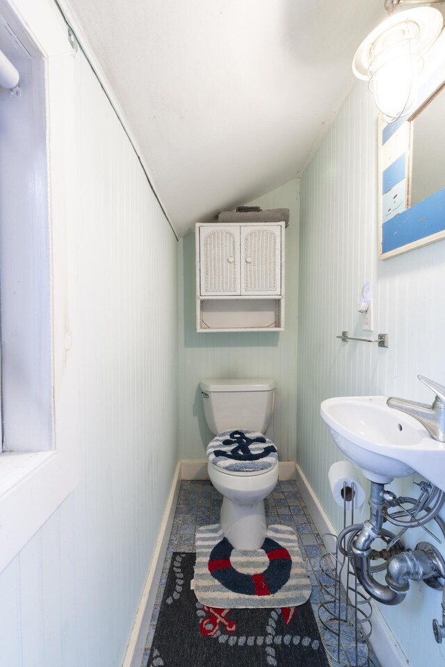 bathroom with wooden walls, toilet, and lofted ceiling