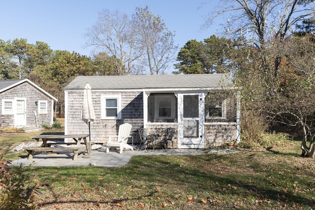 back of property featuring a lawn, an outbuilding, and a patio