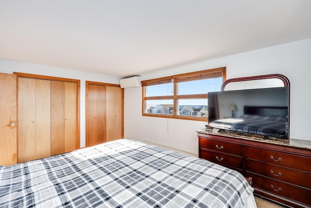 bedroom with a wall mounted air conditioner, light carpet, and multiple closets