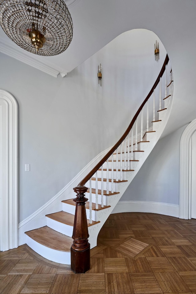 stairs with ornamental molding, a notable chandelier, and baseboards