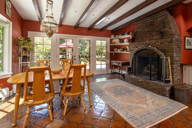 dining space with a notable chandelier, french doors, beamed ceiling, and a brick fireplace