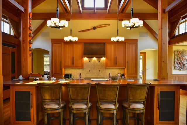 71 Stoney Hill Rd, Tisbury, MA 02568 - kitchen with arched walkways, a chandelier, wall chimney exhaust hood, beamed ceiling, and decorative backsplash