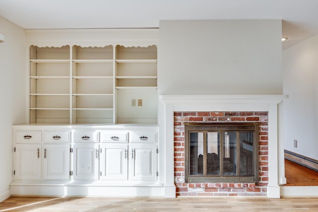 unfurnished living room with a brick fireplace, a baseboard heating unit, and light hardwood / wood-style flooring