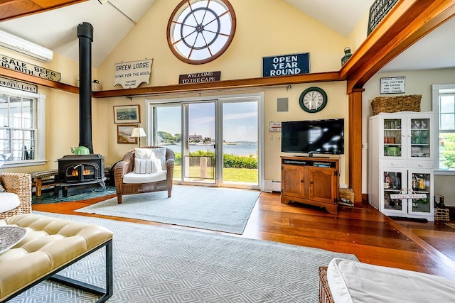 living room with a wood stove, a healthy amount of sunlight, high vaulted ceiling, and wood finished floors