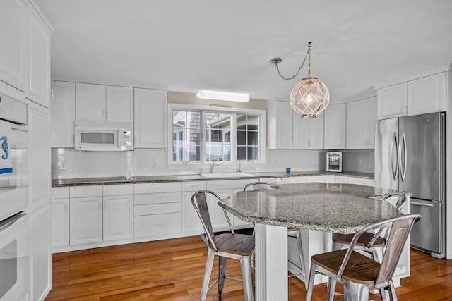 7 Dunes Rd, Harwich Port, MA 02646 - kitchen with freestanding refrigerator, white microwave, a kitchen breakfast bar, backsplash, and white cabinets