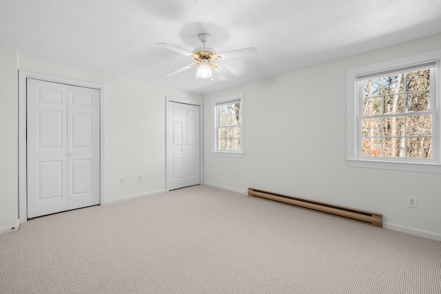 unfurnished bedroom featuring a baseboard heating unit, multiple closets, light colored carpet, and baseboards