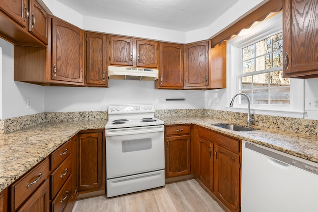 kitchen with white appliances, light stone countertops, a sink, light wood-style floors, and under cabinet range hood