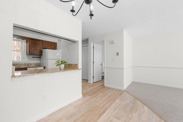 kitchen with light wood-type flooring, a notable chandelier, light stone counters, white appliances, and baseboards