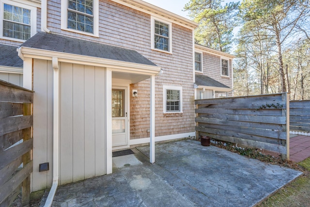 rear view of property with a patio, roof with shingles, and fence