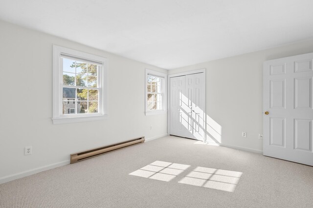 unfurnished bedroom with a closet, baseboard heating, baseboards, and carpet floors