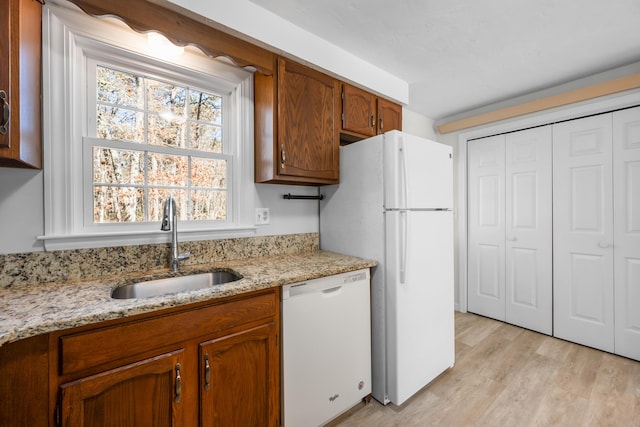 kitchen with white appliances, light stone counters, brown cabinets, a sink, and light wood-type flooring