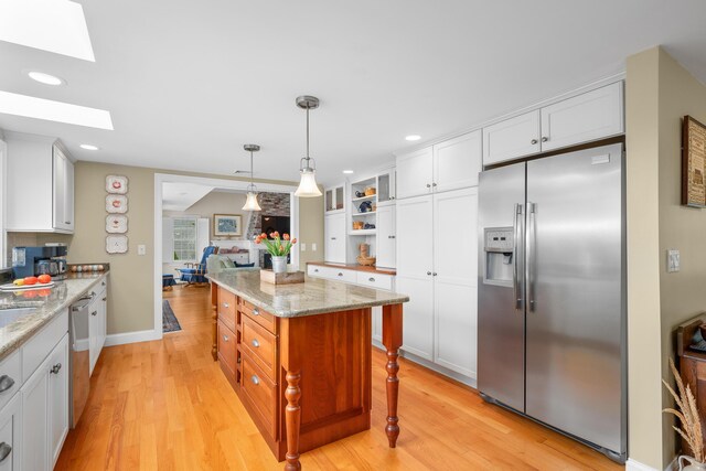 kitchen with stainless steel appliances, a skylight, light wood-style flooring, recessed lighting, and light stone countertops