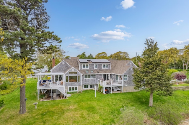 rear view of property with stairs, a wooden deck, roof mounted solar panels, and a lawn