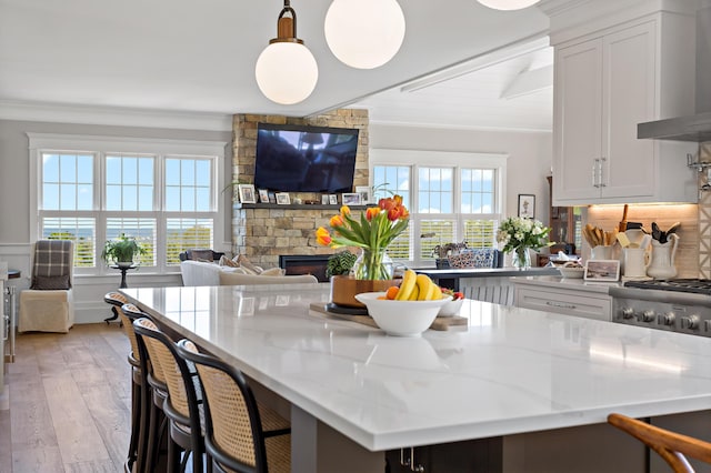 27 Gully Ln, East Sandwich, MA 02537 - kitchen featuring wall chimney range hood, a stone fireplace, white cabinetry, light stone counters, and light wood finished floors