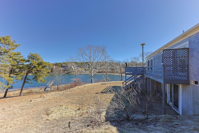 view of yard featuring stairway and a deck with water view