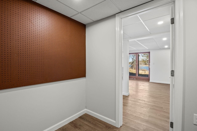 corridor featuring a paneled ceiling, baseboards, and wood finished floors