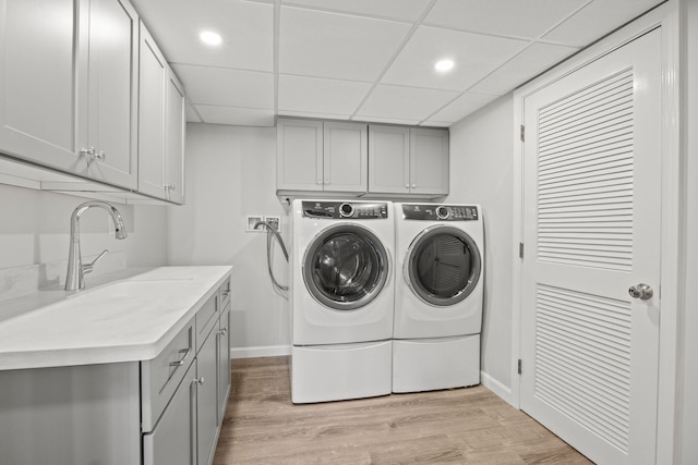 laundry room featuring cabinet space, light wood-style floors, a sink, separate washer and dryer, and baseboards