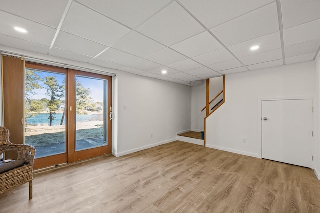 below grade area with stairway, a paneled ceiling, light wood-style flooring, and baseboards