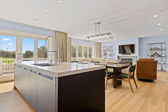 kitchen with a high end fireplace, light wood-type flooring, french doors, pendant lighting, and an island with sink