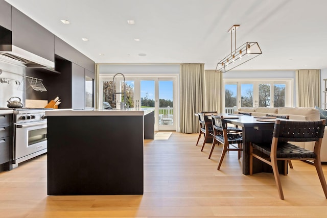 kitchen featuring light hardwood / wood-style floors, hanging light fixtures, french doors, high end stainless steel range oven, and an island with sink