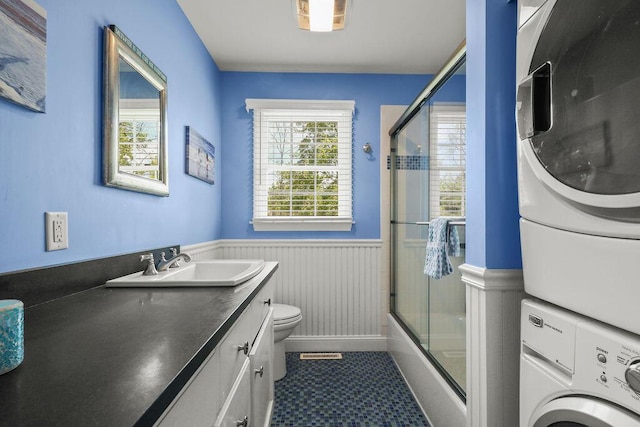 33 Beach Rd, Orleans, MA 02653 - bathroom featuring stacked washer and clothes dryer, a wainscoted wall, toilet, vanity, and shower / bath combination with glass door